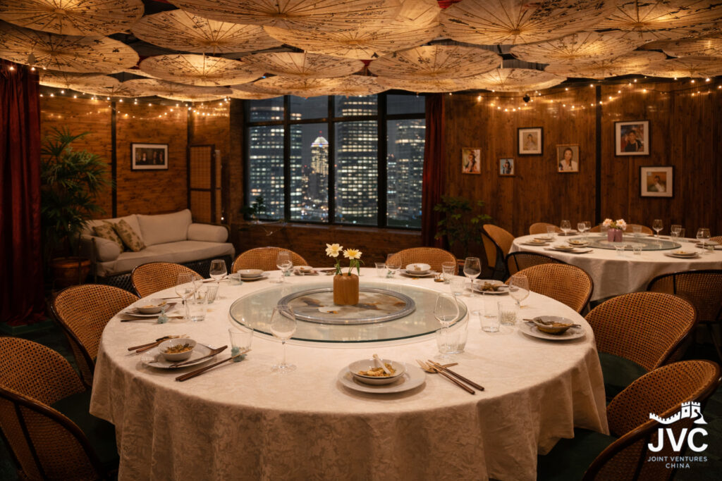 Formal private dining room after a business dinner in China, showing an empty round table with a lazy susan, place settings, and a city skyline visible through the window.